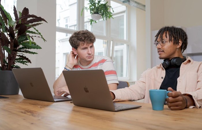 Two young men seated at a table, focused on their laptops, indicating a productive work session.